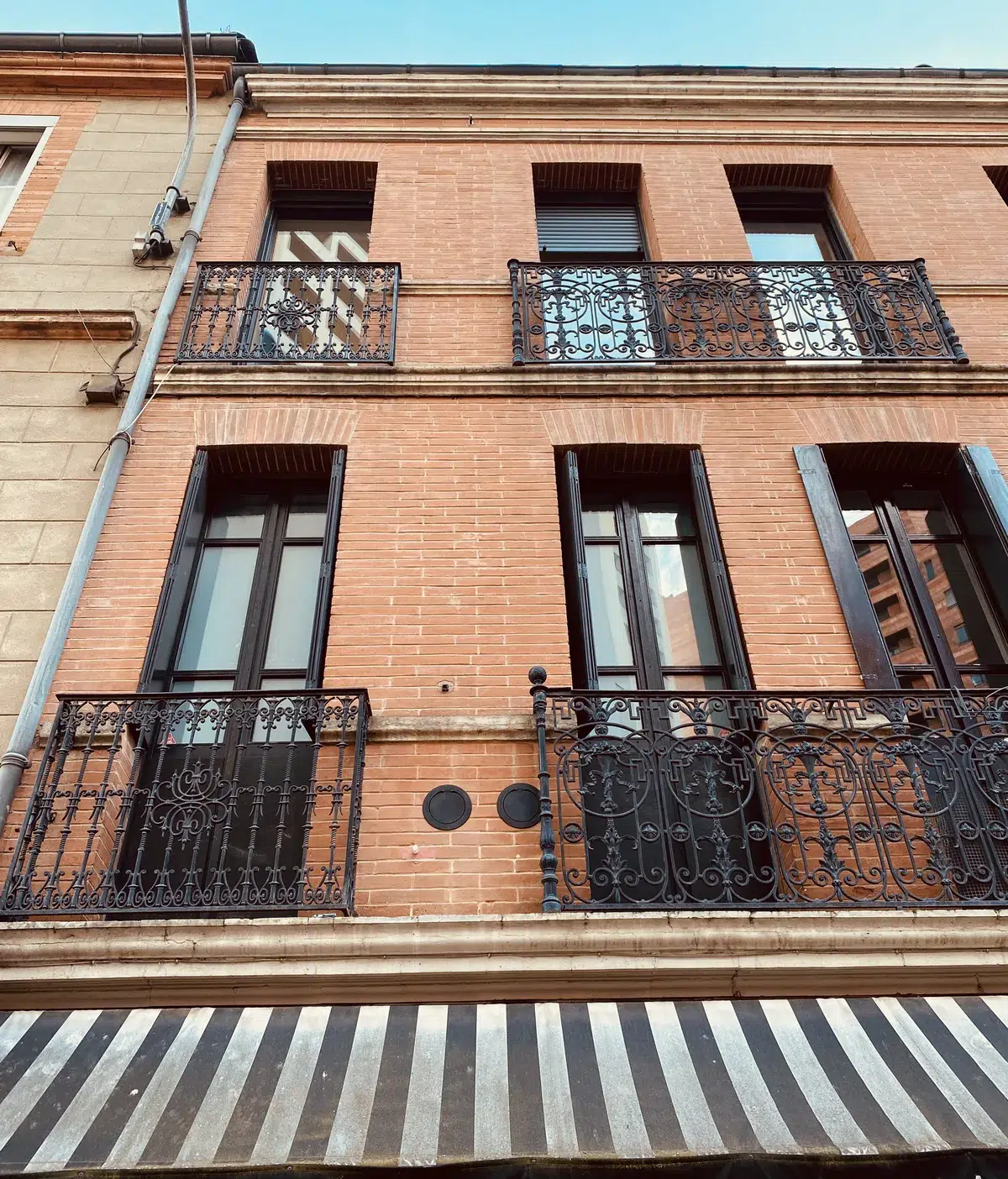 Façade d’un commerce toulousain équipé par ATM Monoclim : deux grilles rondes entre les balcons